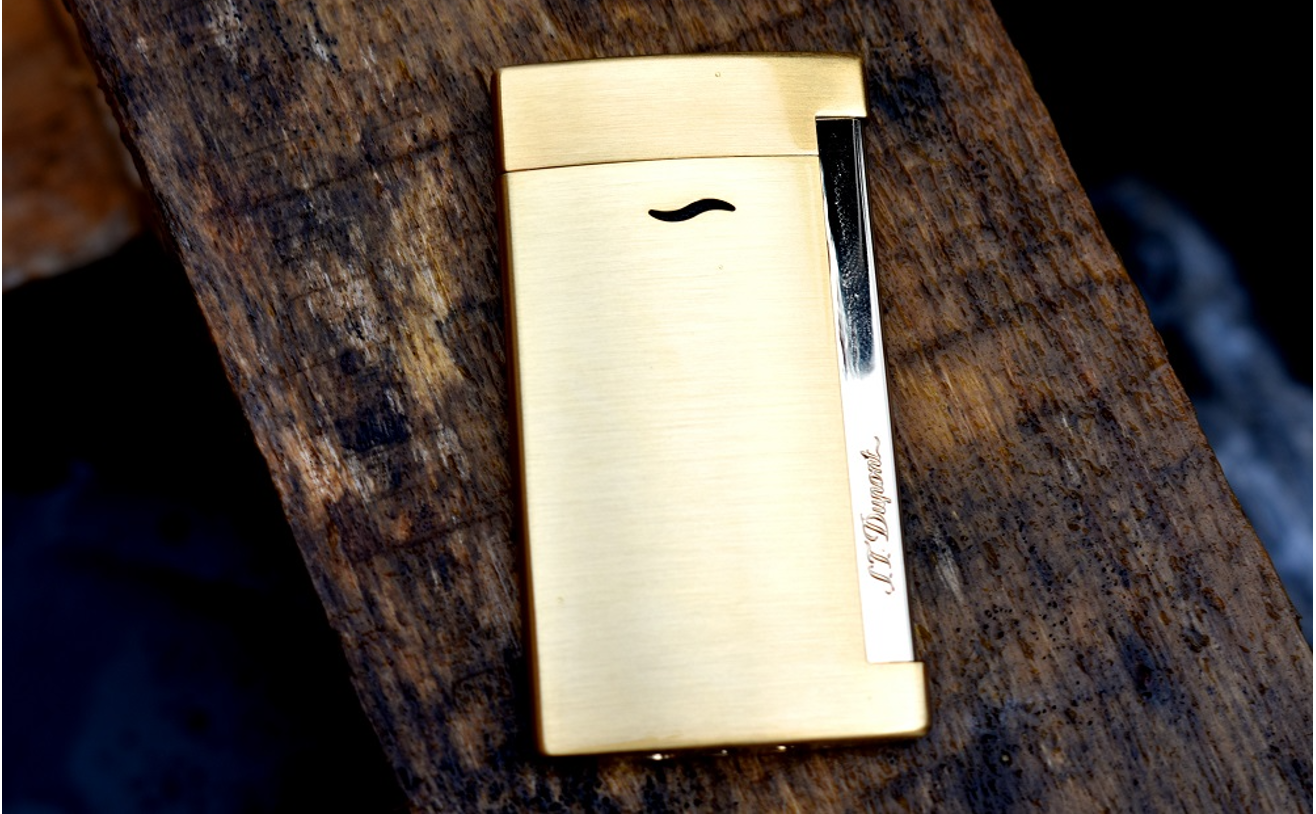S.T. Dupont Slim 7 torch lighter with brushed gold finish and chrome ignition trigger on a wooden background.