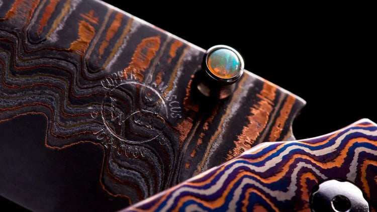 Close up of William Henry folding knife showcasing Mokume-gane decorated handle and copper wave damascus blade.