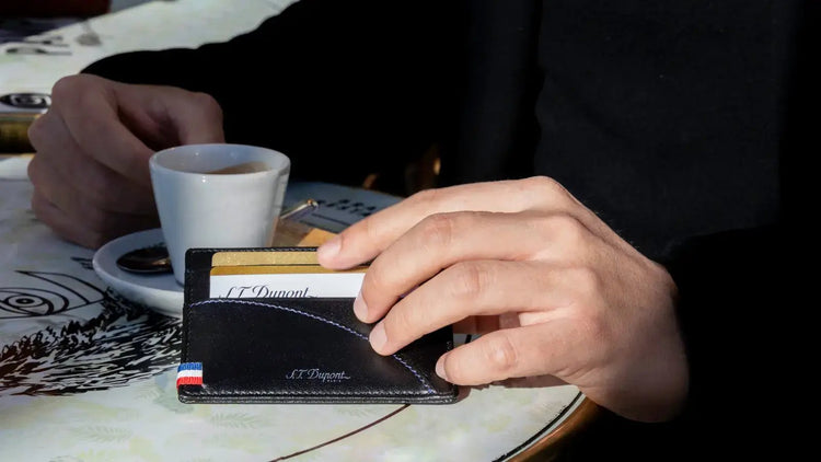 Man with coffee holding S.T. Dupont leather credit card holder with S.T. Dupont signature logo and blue, white, and red threads symbolizing the French flag