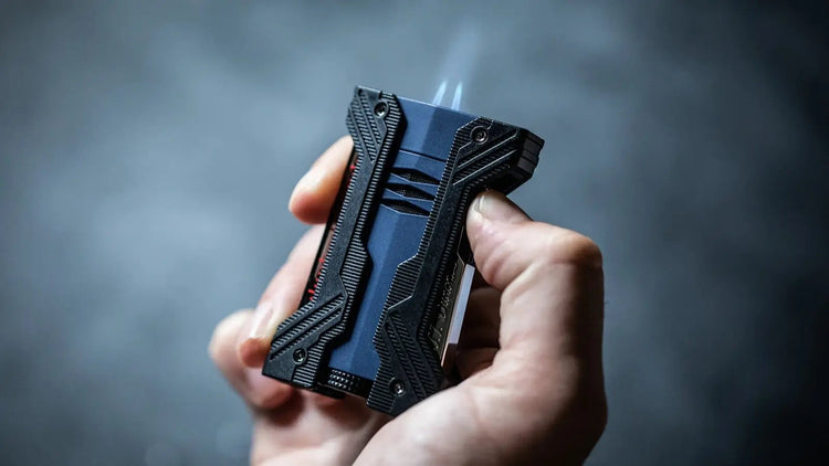 S.T. Dupont Defi XXtreme double flame torch lighter with deep matte blue coloring and black bumpers behind ignited in hand.