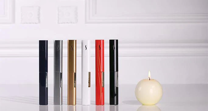 S.T. Dupont Wand candle lighter in black, gunmetal, gold, white, red with gold accents and shiny black standing next to a burning round candle.