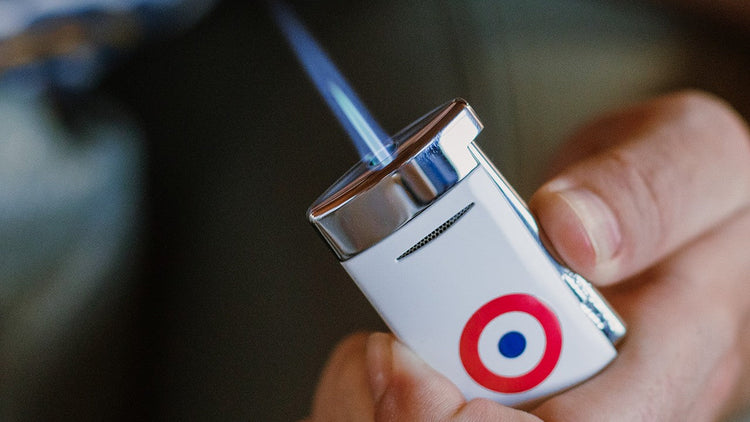 S.T. Dupont Minijet torch lighter with white lacquer and red and blue rosette pattern being ignited in hand.