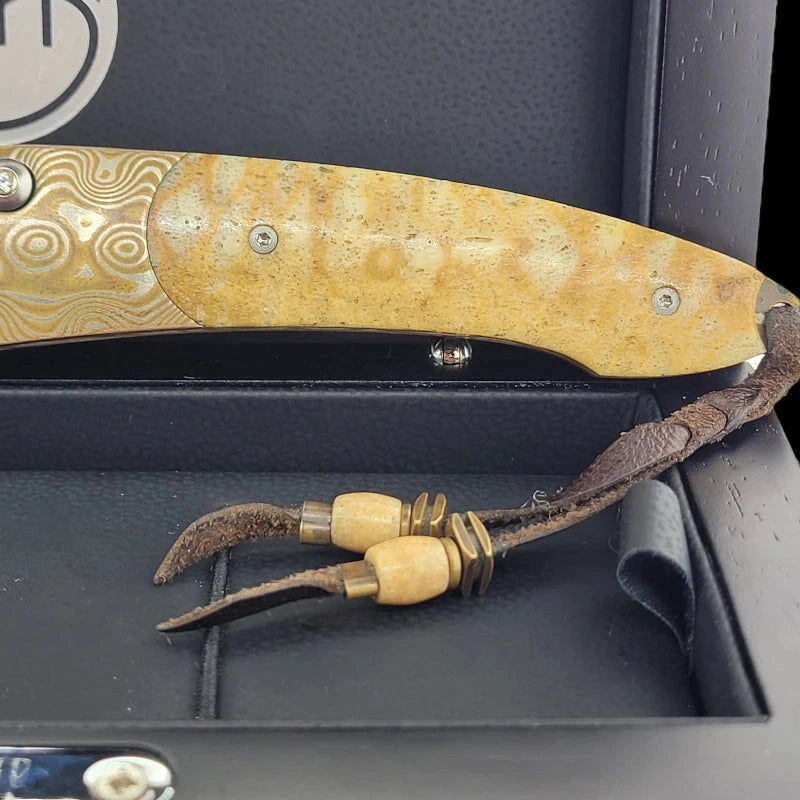 Close-up of the William Henry B7 knife's Tiger Coral handle and braided leather lanyard with gold and silver accents inside a display box.