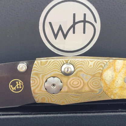 Detailed view of the William Henry B7 knife's Mokume-Gane frame and lock button adorned with white topaz, set against the dark interior of the box